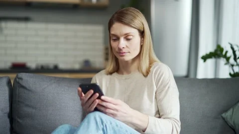 Caucasian woman using smartphone while sitting on sofa in living room at home.  Stock Footage 231224807