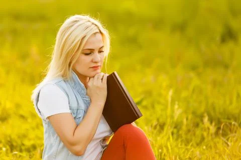 A Caucasian young Christian woman reading a Bible outdoors in a public park. Stock Photos