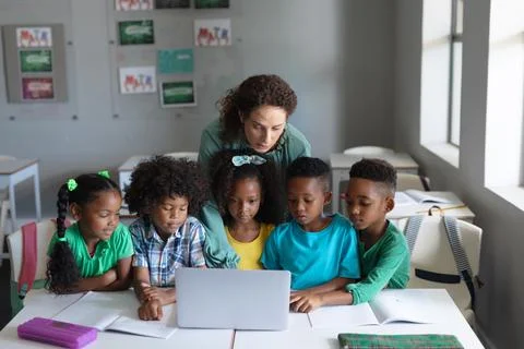 Caucasian young female teacher teaching laptop to african american elementary Stock Photos