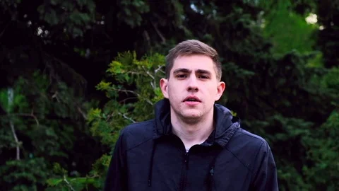 Caucasian young guy in a black jacket walks in the park and talks to the camera Stock Footage 129688409