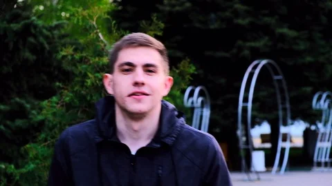 Caucasian young guy in a black jacket walks in the park and talks to the camera Stock Footage 129688413