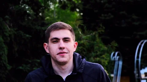 Caucasian young guy in a black jacket walks in the park and talks to the camera Stock Footage 129688443