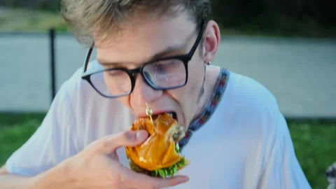 Caucasian young guy eats meat burger with pleasure, on fast food restaurant Stock Footage 283359561