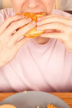 Caucasian young man eats half-eaten sesame fresh hamburger Stock Photos