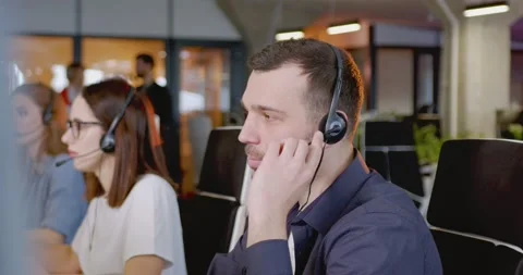 Caucasian young man in headset talking with client at computer. Call center Stock Footage 179959133