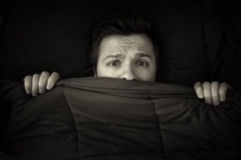 Caucasian young man hiding in bed under the blanket at home. 스톡 사진