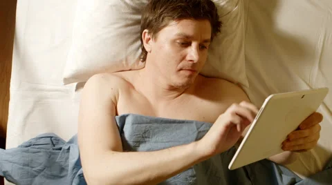 Caucasian young man types a tablet PC in a bed Stock Footage 66748155