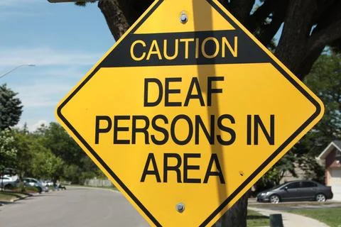 Caution deaf persons in area diamond sign in black writing on yellow background Stock Photos