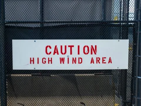Caution high wind area sign handing on black fence Stock Photos