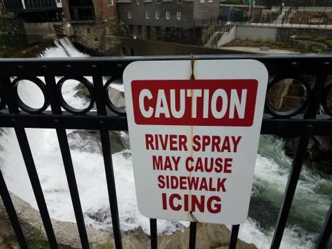Caution river spray may cause sidewalk icing sign and river Stock Photos