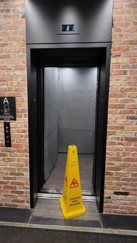Caution Sign Blocking Elevator Entrance in Modern Brick Hallway of NYC Building Stock Footage 334671671