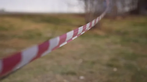 Caution tape billowing softly, blocking blurred outdoor scene, symbolizing Stock Footage 308055096