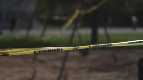 Caution tape surrounding an empty playground with skateboarders out of focus Video stock 130389478