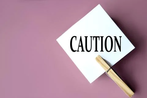 CAUTION - word on white sheets of paper with clothespins on a coffee backgrou Stock Photos