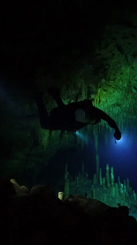 Cave diver with flashlight exploring a dark underwater grotto with stalactites Stock Footage 331340541
