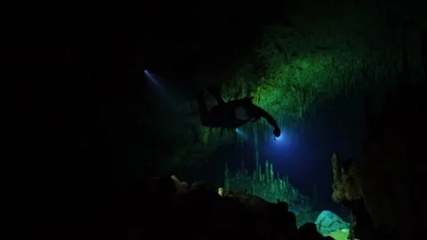 Cave diver with flashlight exploring a dark underwater grotto with stalactites Vídeos de archivo 331340605