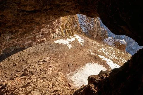 Cave opening with a view of a mountain slope covered with rocks and patches.. Stock Photos