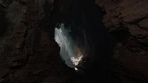 A cave with a stunning ray of light shining through a large hole in the ceili Stock Illustration