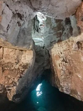 Cave with turquoise pool, rough stone walls, and a small light opening. Stock Photos