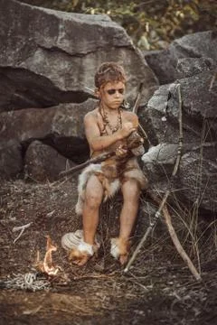 Caveman, manly boy making primitive stone weapon in camp Stock Photos