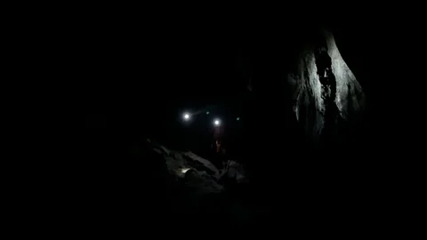 Cavers searching shining their head lamp around inside cave Stock Footage 122099899