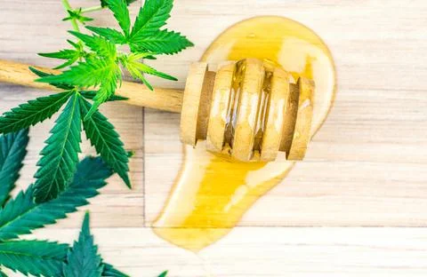 CBD Cannabis infused Honey with dipper spoon jar Marijuana leafs on wooden ta Stock Photos