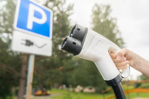 CCS2 charging plug held in a hand beside an electric vehicle parking sign a.. Stockfoto's