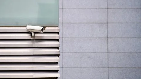 CCTV camera on the facade of the white building with ventilation grate Stock Photos