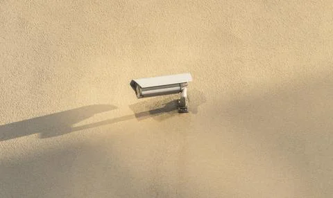 A CCTV camera hangs on the corner of a beige building Stock Photos