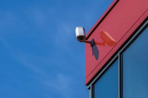 CCTV camera on modern building. Security camera on red wall, blue sky backgro Stock Photos