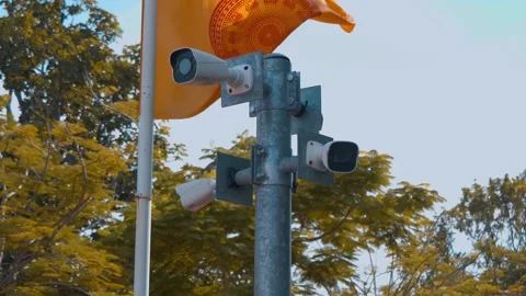 CCTV cameras fixed on a pole spy on everyone around and a Thai Buddhist flag  Stock Footage 308894463