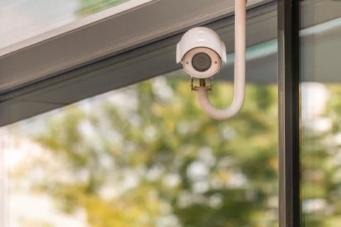 CCTV or surveillance camera operating on window building with green trees fol Stock Photos
