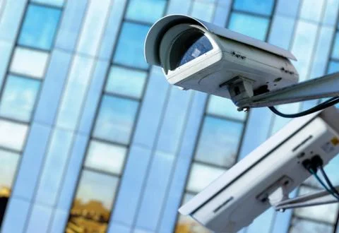 Cctv security camera in a city with blury business building on background Stock Photos