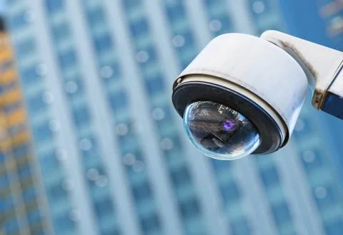 Cctv security camera in a city with blury business building on background Stock Photos