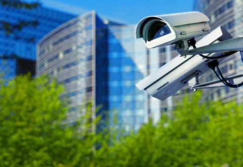 Cctv security camera in a city with blury business building on background Stock Photos