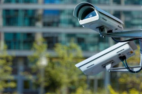 Cctv security camera in a city with blury business building on background Stock Photos