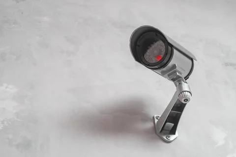 CCTV security camera with a glowing red light is mounted on a gray wall. Se.. Stock Photos