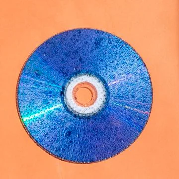 CD disk with water drops on shiny surface against orange background Stock Photos