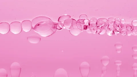 Cear bubbles form and float to another on pink liquid surface Video stock 233816926