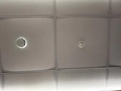 Ceiling with circular smoke detector and speaker grid pattern suitable for .. Foto stock