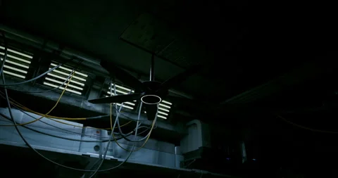 Ceiling fan spins in a dimly lit industrial space surrounded by wires Stock Footage 305695236