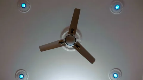 The ceiling fan with three blades begins to rotate on a white ceiling with burni Stock Footage 108126910