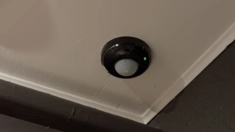 Ceiling mounted motion sensor with green indicator light on interior corner Stock Footage 347514419