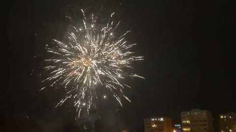 Celebratory fireworks explode over cityscape amid glowing embers and smoke Stock Footage 334117997
