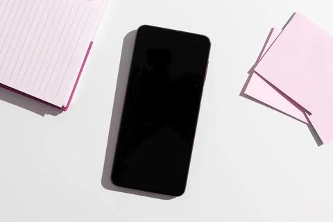 Cell phone next to a stack of pink sticky notes and a pink notebook, with copy s 库存照片
