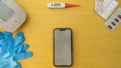 A cell phone is on a table next to a thermometer and a blood pressure cuff Stock Photos