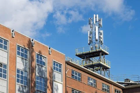A cell phone tower with multiple antennas sits atop a red brick building agai Stock Photos