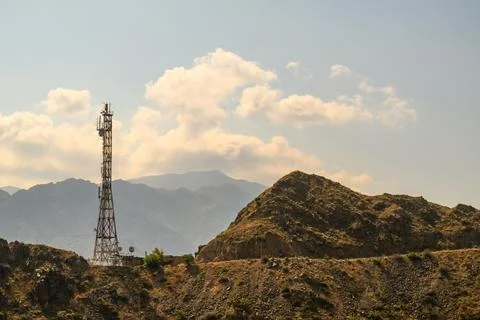 Cell tower rises above arid mountains with scattered clouds Stock Photos
