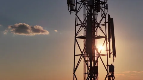 Cell tower silhouette against a sunset sky with a small cloud, representing Stock Footage 345502757