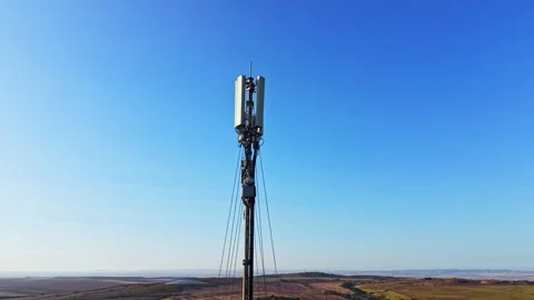 Cell tower stands tall against a clear blue sky in a vast open landscape with 스톡 동영상 344778102